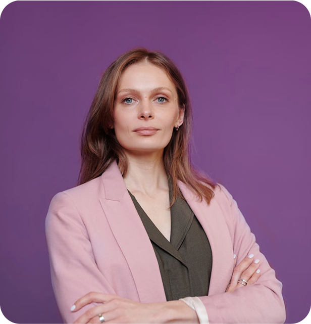A woman in a pink blazer, arms crossed, smiling confidently.